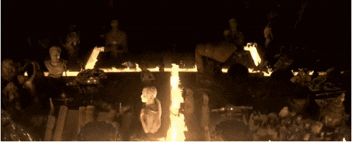 a group of people are standing around a cross in a dark room surrounded by flames .