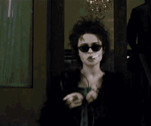 a woman wearing sunglasses is smoking a cigarette in front of a door
