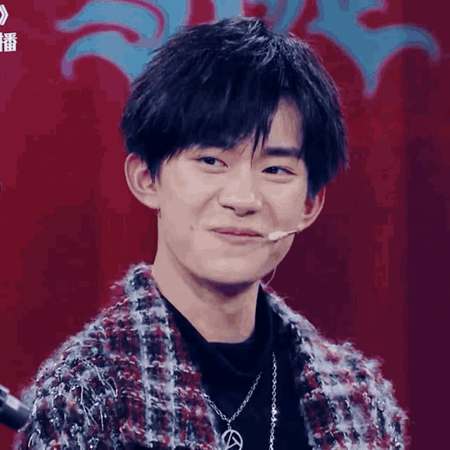 a young man wearing a plaid jacket and a necklace is making a face