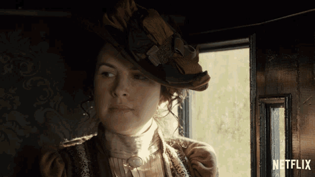 a woman wearing a hat looks out a window with netflix written on the bottom right