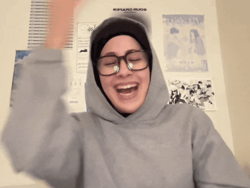 a woman wearing glasses and a hooded sweatshirt is laughing in front of a poster that says edward rudo