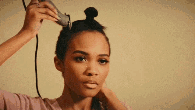 a woman is cutting her hair with a clipper and looking at the camera .