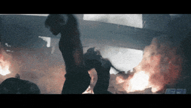 a man in a black tank top stands in front of a fire