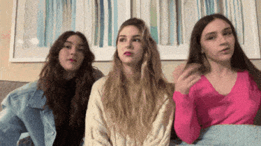 three girls are sitting on a couch and one of them is wearing a pink shirt
