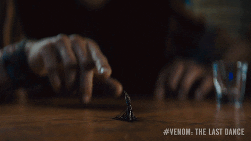 two men are sitting at a bar with #venom the last dance on the bottom