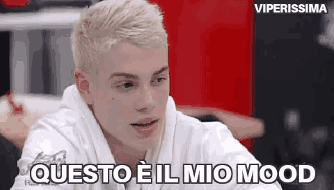 a young man with blonde hair is wearing a white hoodie and talking to someone .