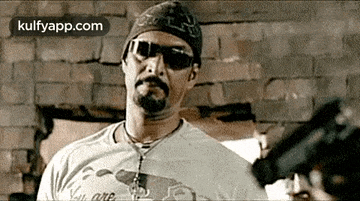 a man wearing sunglasses and a bandana is holding a gun .