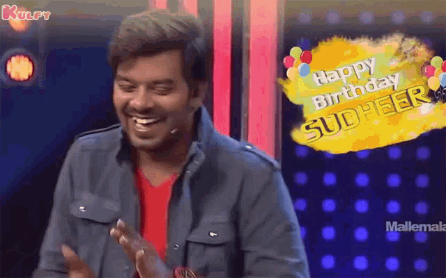 a man is laughing and clapping in front of a sign that says happy birthday sudheer