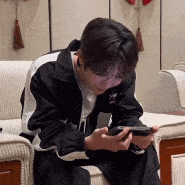 a man sitting on a couch looking at his phone with a jacket that says mw on it