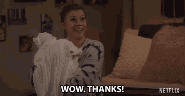 a woman in a tie dye sweater is holding a white blanket and says wow thanks