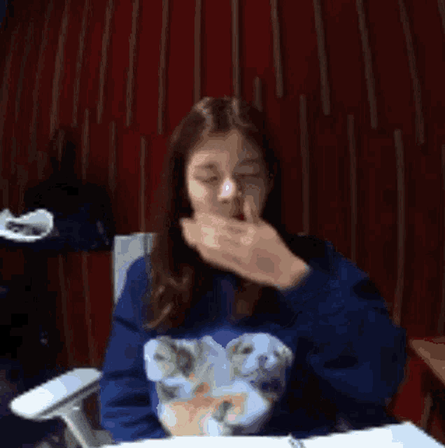 a woman wearing a blue sweater with a bear on it covering her mouth with her hand