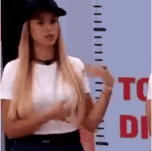 a woman in a white shirt and black hat is standing in front of a measuring tape .