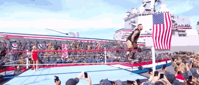 a man is jumping over a rope in a wrestling ring in front of a large american flag .