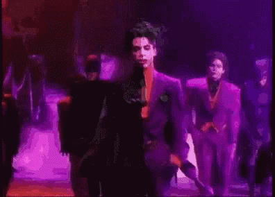 a man in a purple suit is dancing on a stage with a group of people .