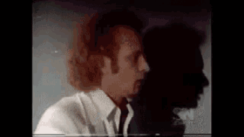 a man in a white shirt and tie is looking at his reflection in a dark room .