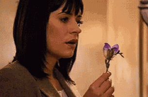 a woman is holding a purple flower in her hand and smelling it .