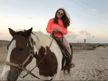 a woman wearing sunglasses is riding a brown and white horse on a sandy beach