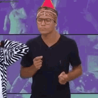 a man wearing a party hat and glasses is dancing in front of a zebra .