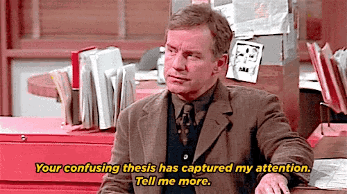 a man in a suit and tie is sitting at a desk and says " your confusing thesis has captured my attention tell me more "