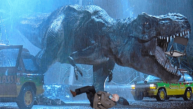 a man is laying on the ground in front of a dinosaur and a jurassic park car
