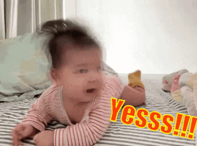 a baby is laying on its stomach on a bed with the word yesss written on it .