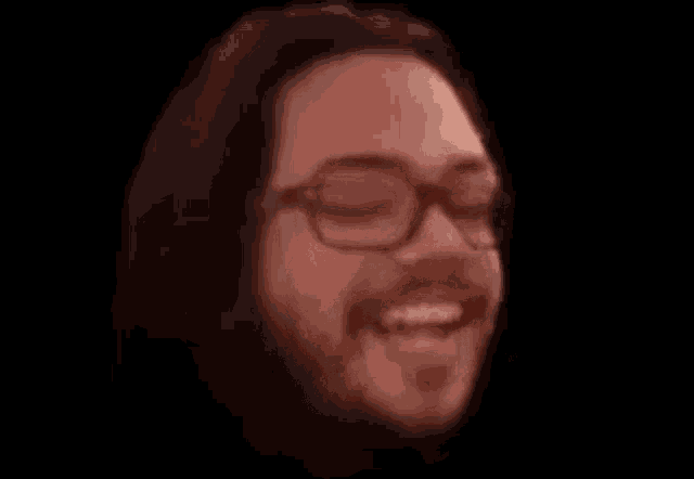 a man with long hair and a beard wearing glasses is smiling .
