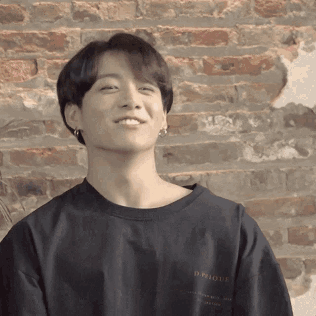 a young man wearing a black shirt with the word desigual on the back is smiling in front of a brick wall