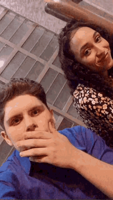 a man and woman are posing for a picture and the man is covering his mouth with his hand