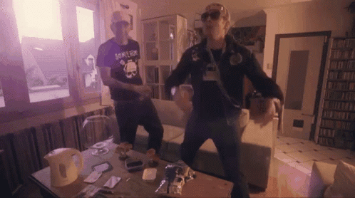 two men are dancing in a living room and one has a shirt that says joker