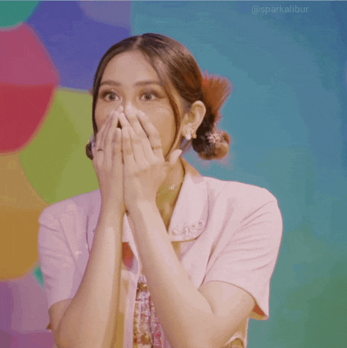 a woman covering her mouth with her hands in front of a colorful backdrop