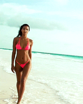 a woman in a pink bikini walks on the beach