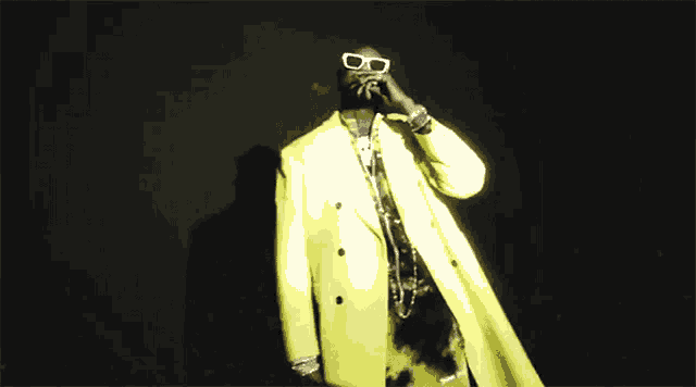 a man in a yellow suit and sunglasses is smoking a cigarette in a dark room .
