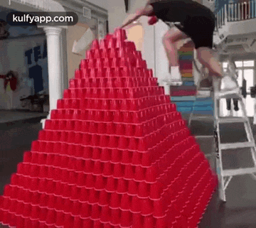a man is jumping over a stack of red cups .