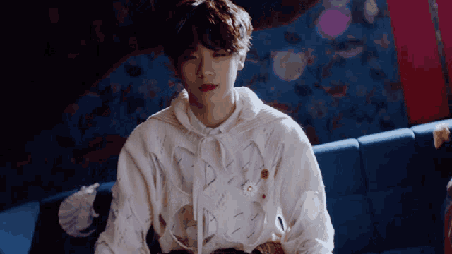 a young man wearing a white sweater with holes in it sits on a blue couch
