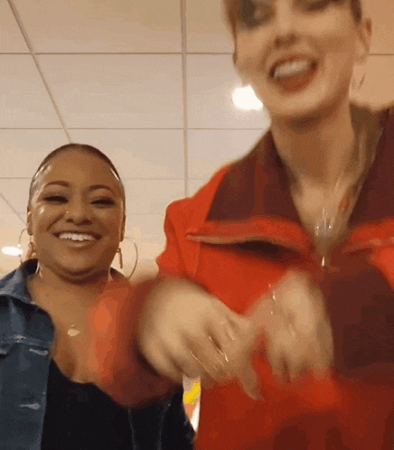 a woman in a red jacket is smiling next to another woman in a black shirt