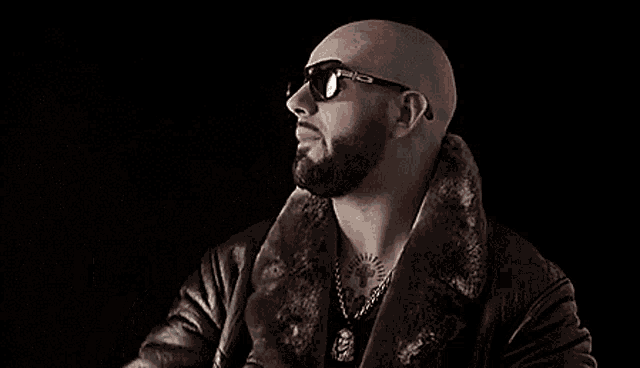 a bald man with a beard and sunglasses is wearing a leather jacket and fur collar .