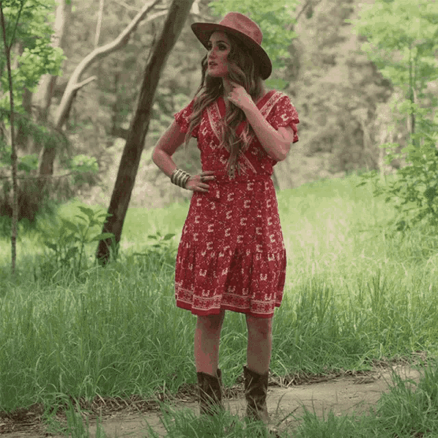 a woman wearing a red dress and cowboy boots stands in a field