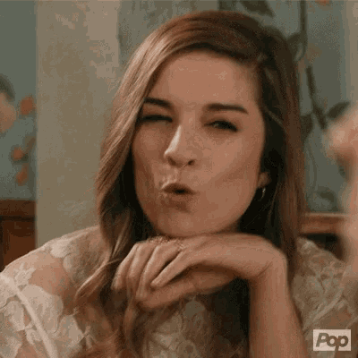 a woman in a white lace dress is blowing a kiss with her hand on her chin .