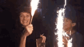 a woman is holding a sparkler in front of her face while another woman holds a sparkler in front of her face .