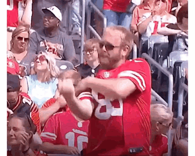 a man in a red jersey with the number 18 on it is standing in a crowd of people .