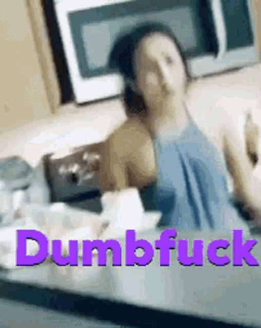 a woman is sitting at a table with a microwave in the background and the words dumbfuck written in purple .