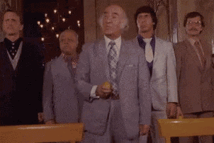 a group of men in suits and ties are standing in a room . one man is holding a yellow object in his hand .