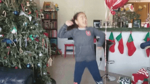 a girl dancing in front of a christmas tree and stockings