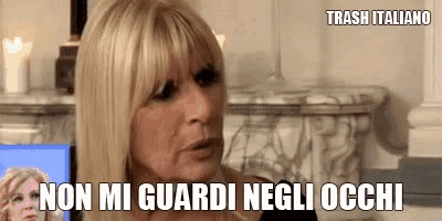 a woman with blonde hair and bangs is sitting in front of a fireplace and says non mi guardi negli occhi