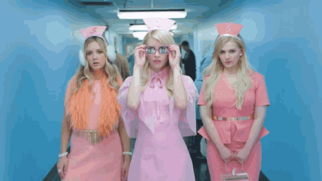 three women dressed in pink nurse outfits are walking down a hallway