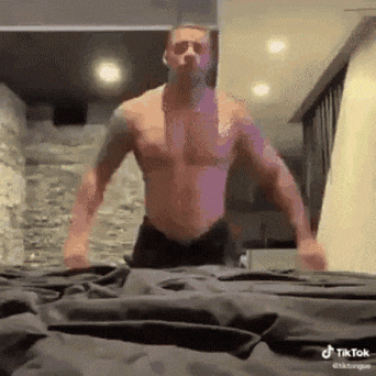 a shirtless man is standing on top of a bed with his arms outstretched .