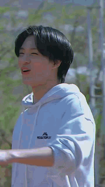 a young man wearing a white hoodie is standing in front of a building and smiling .