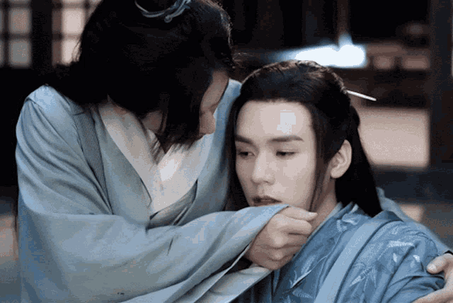 a man is touching another man 's face while wearing a blue robe