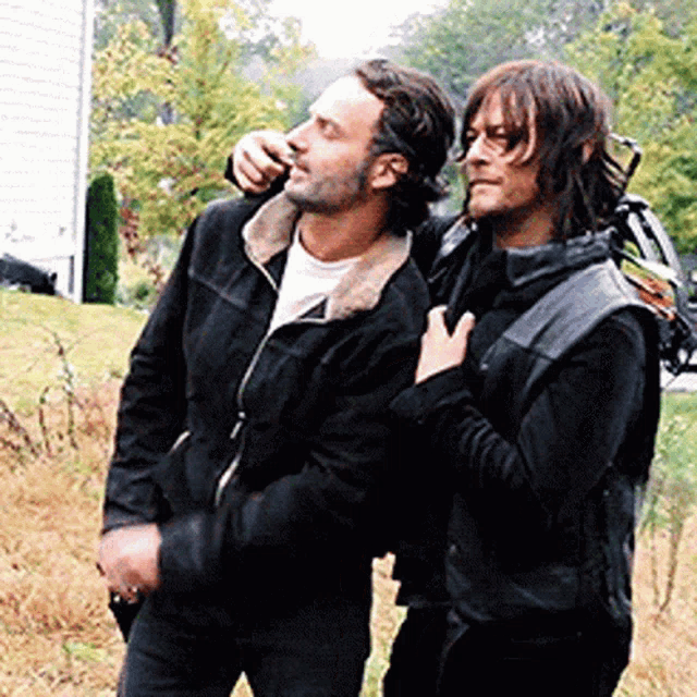 two men are standing next to each other in a field . one of the men is holding the other 's hand .