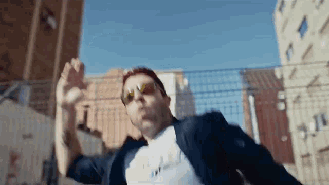 a man in a suit and sunglasses is dancing in front of a building .